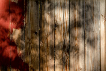 Weathered brown wood background surface with red paint. Wooden wall texture planks with tree shadow.