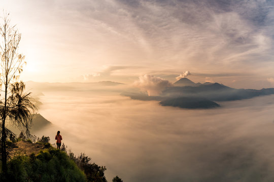 A young woman standing on the edge of a giant cliff, overlooking Mount Bromo and the Tengger Crater