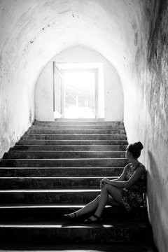 A woman sitting on stairs in a tunnel looking towards the doorway