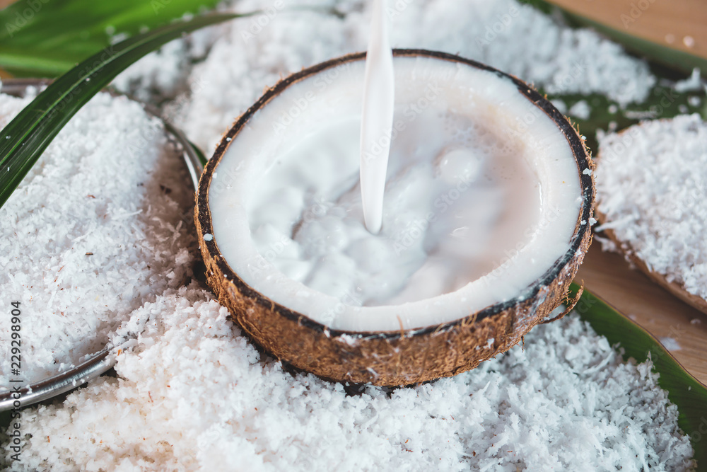 Wall mural pouring fresh coconut milk and coconut fruit ingredient on wooden table 