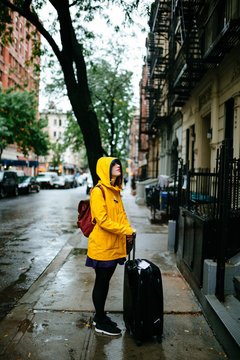 a woman in the streets of new york with a yellow raincoat and a suitcase