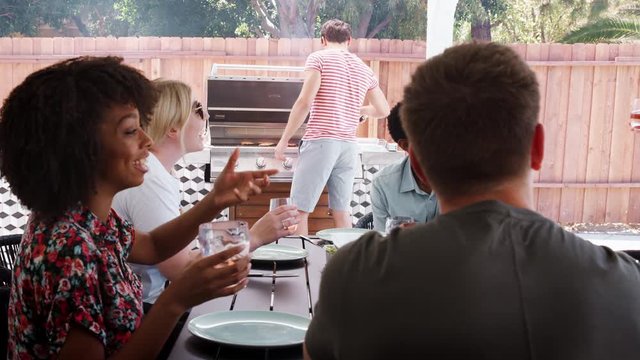 Young adult friends sitting outdoors barbecuing