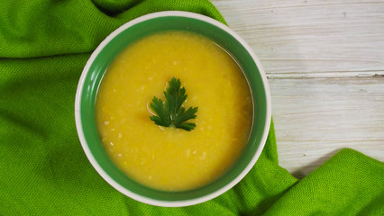 Delicious pea puree soup on green napkin and wooden background.
