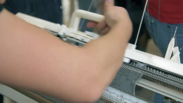 Close up female hands working on modern knitting machine. Knitting yarn on weaving machine. Knitting machine production cloth