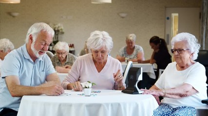 Group Of Seniors Playing Game Of Bingo In Retirement Home