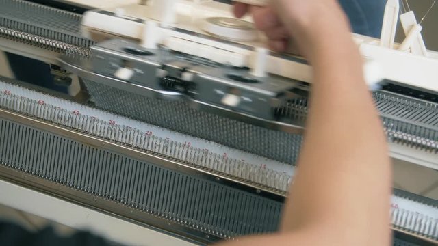 Close up female hands working on modern knitting machine. Knitting yarn on weaving machine. Knitting machine production cloth