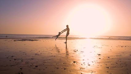 Ultra slow motion - silhouette of father and son playing together in the beach at sunset