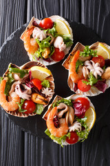 Fresh seafood salad with vegetables and lemon served in seashells close-up. Vertical top view