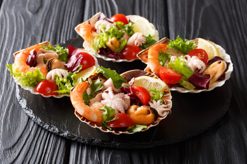 Seafood appetizer salad of shrimp, octopus, mussels, squids and scallops with vegetables and lemon in seashells close-up. horizontal