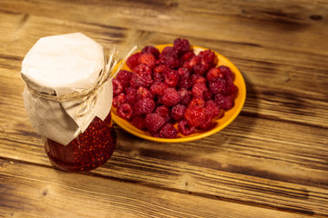 Raspberry jam in glass jar and fresh raspberries on wooden table