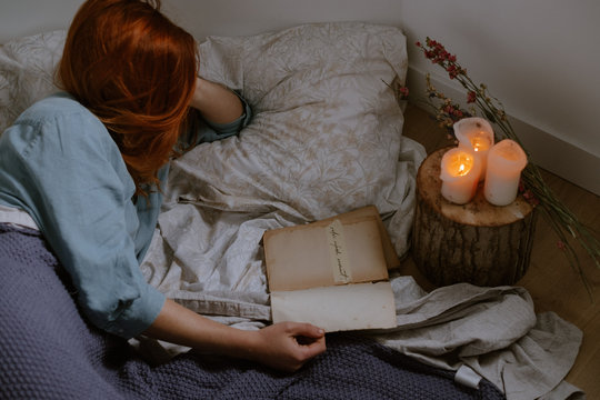 woman reading on bed close to candles