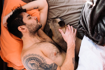 A caucasian man and a brown french bulldog cuddling together in bed