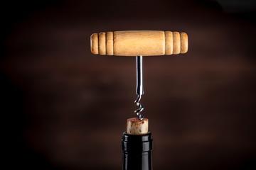 A side view of a vintage corkscrew in a bottle of wine, on a dark background with copy space
