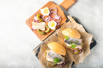 Sandwich with herring fillets, onion, eggs, pickled cucumber on parchment paper on board. Traditional street food in norway or sweden. Top view