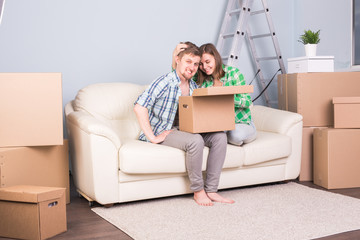 Real estate, relocation and moving concept - young couple holding a cardboard sitting on sofa