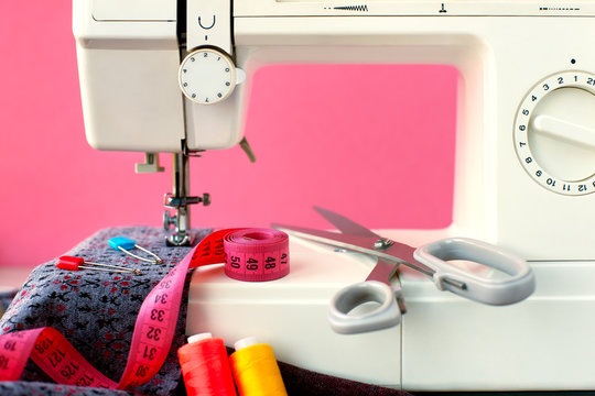Sewing machine and cloth on a pink background. Sew clothes on a sewing machine from knitting fabric. Fabric, measuring tape, thread, scissors and sewing machine on a pink background.