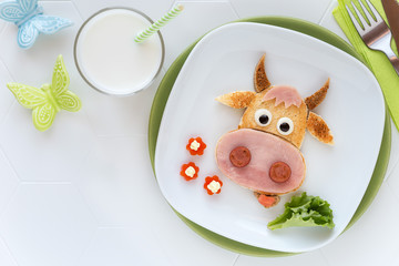 Fun food for kids - cute cow shaped sandwich with ham sausages served with a glass of milk for breakfast or dinner