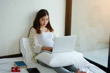 Pregnant woman is using laptop computer on bed.