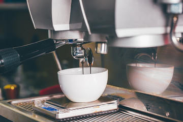 Coffee extraction pouring into a cup from professional coffee machine with bar interior background