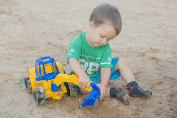 little boy playing with toy excavator in the sand. The child sits in the sand and plays with the typewriter.