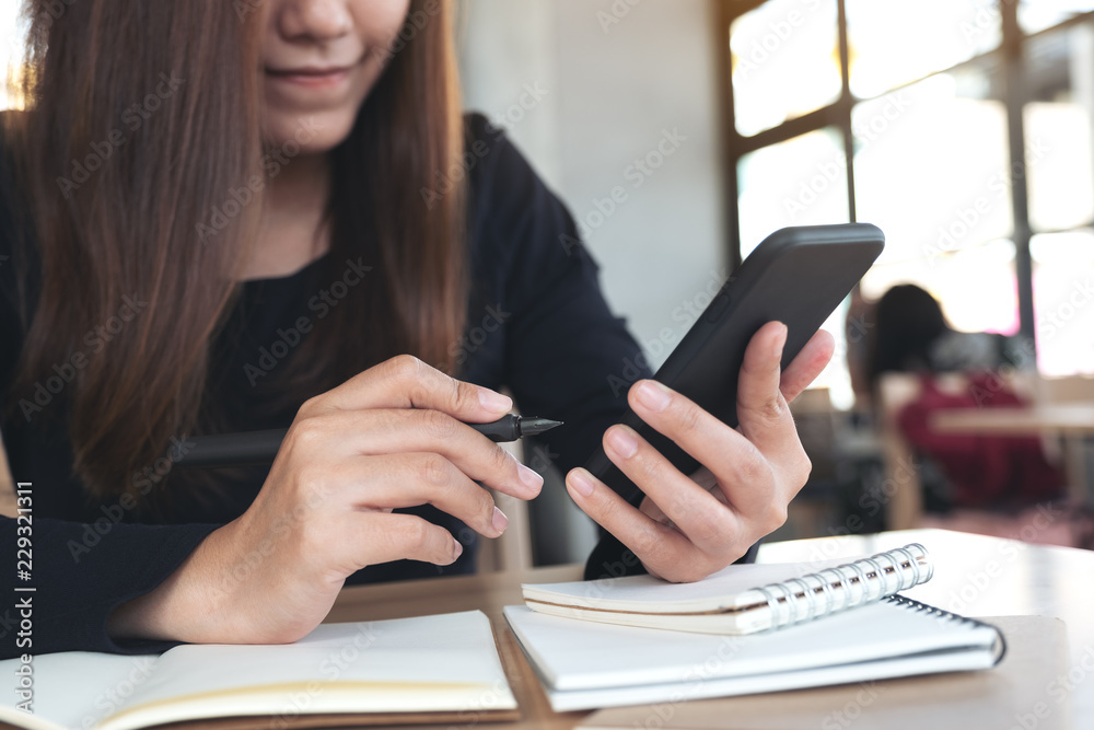 Canvas Prints closeup image of an asian woman holding , using and looking at smart phone while working and writing