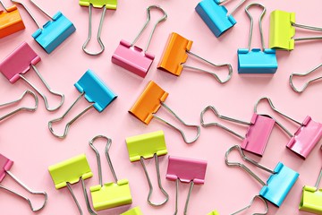 Business, office supplies, teamwork, corporation, collaboration or unity concept : Top view or flat lay of multi colored binder clips on pink background