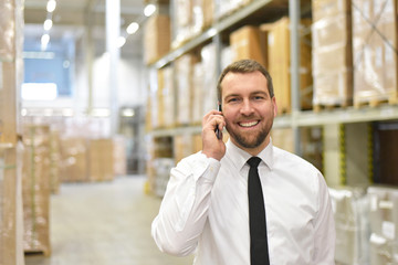 Happy businessman makes a phone call in the warehouse of a logistics company // fröhlicher...