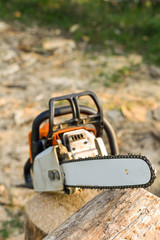 Naklejka premium Chainsaw that stands on a heap of firewood in the yard on a beautiful background of green grass and forest.