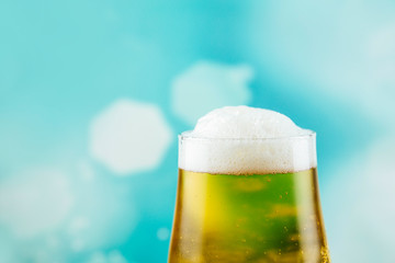 Goblet style beer glass on dark natural wooden table with light blue bokeh background. 
