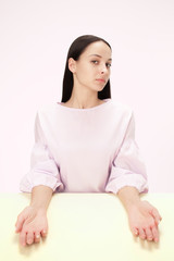 Serious business woman sitting at table on a pink studio background. The portrait in minimalism style