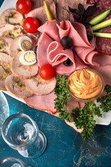 Cold smoked meat plate with prosciutto, salami, bacon, pork chops, cheese and olives on gray stone background.