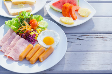 breakfast set fried egg, ham, sausages, fresh vegetable salad and fruit watermelon, pineapple, papaya and bread on rustic wooden table in morning time. Food and drink concept with copy space.