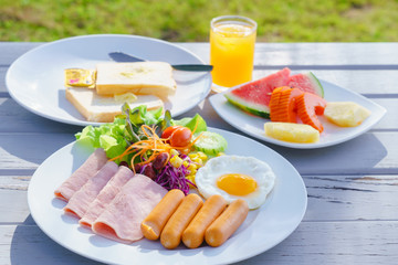 breakfast set fried egg, ham, sausages, fresh vegetable salad and fruit watermelon, pineapple, papaya, bread and orange juice on rustic wooden table. Food and drink concept.