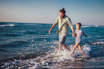 Happy father and son, man & boy child, running and having fun in the sand and waves of a sunny beach