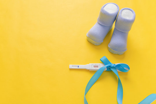 Baby socks and a pregnancy test on a yellow background.