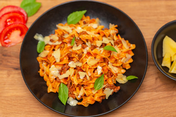 The Pasta Bolognese. Tagliatelle with minced meat, tomato sauce, Basil and Parmesan on a black plate on a dark wooden background.