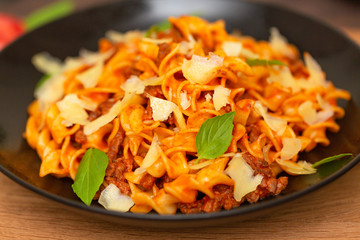 The Pasta Bolognese. Tagliatelle with minced meat, tomato sauce, Basil and Parmesan on a black plate on a dark wooden background.