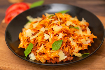 The Pasta Bolognese. Tagliatelle with minced meat, tomato sauce, Basil and Parmesan on a black plate on a dark wooden background.