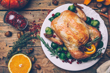 Thanksgiving roasted chicken with Brussels sprouts and spices on a rustic wooden table. Thanksgiving dinner or fall dinner concept background with autumn leaves. Thanksgiving table setting background.