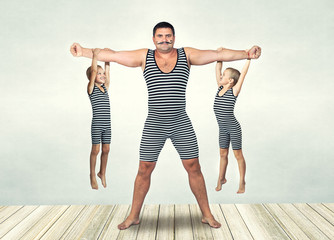 Family of strongman. The father of two sons in vintage costume of athletes perform strength...