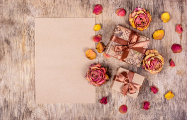 Gift boxes, message and roses on wooden background. Dry flowers, dried roses. Copy space