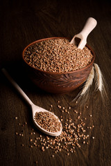 Buckwheat in a wooden bowl on a wooden background near the ears of wheat. wooden spoon with Buckwheat