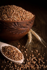 Buckwheat in a wooden bowl on a wooden background near the ears of wheat. wooden spoon with Buckwheat