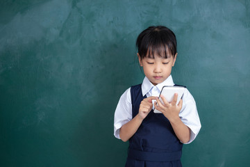 Asian Chinese little Girl in uniform playing digital tablet against green blackboard