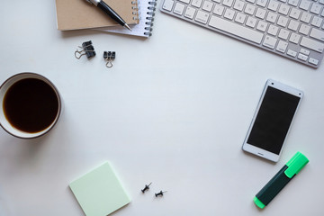 White wooden table with keyboard, pen, notebook, green marker, document clips and a cup of coffee. Workspace top view with copy space.