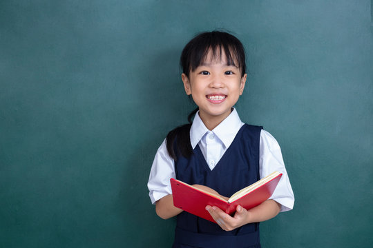 Asian Chinese little Girl in uniform reading book against green blackboard