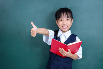 Asian Chinese little Girl in uniform showing thumbs up against green blackboard
