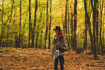 Fototapeta premium Girl of redheads in knitted ethnic ponchos, trousers and a backpack. The warming of the atmosphere is warm and the sun.Portret in the forest. Natural background. Woman travels Travel the photo.