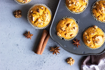 Homemade pumpkin muffins in black baking dish with walnuts and fall spices (anise and cinnamon) over grey concrete background. Traditional autumn and winter baked pastries. Copy space.