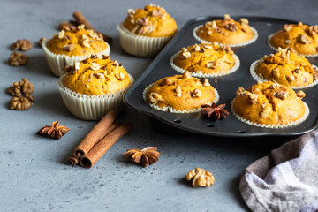 Homemade pumpkin muffins in black baking dish with walnuts and fall spices (anise and cinnamon) over grey concrete background. Traditional autumn and winter baked pastries. Copy space.
